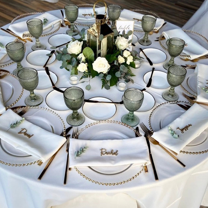 Round tablescape with green glasses, beaded plates, and gold silverware